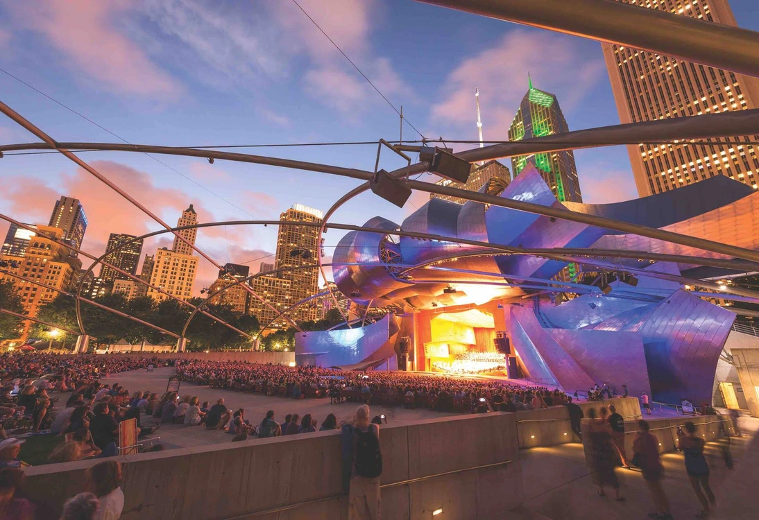 Outdoor evening concert at Jay Pritzker Pavilion, Millennium Park, Chicago with audience and city skyline.