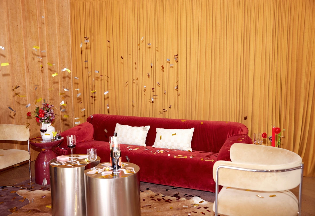 Living room with red velvet sofa, beige chairs, gold curtains, and metallic coffee tables with decorations.