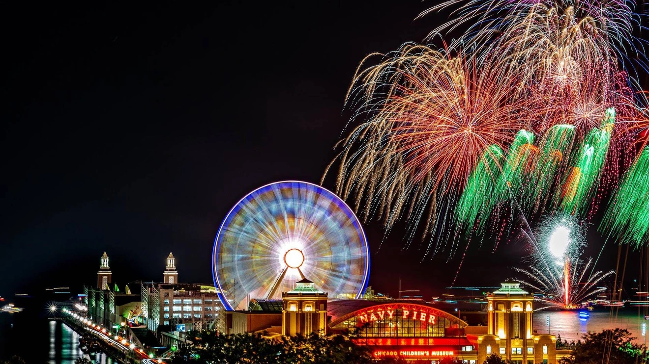 Nighttime fireworks display over Navy Pier with a lit Ferris wheel and illuminated buildings.