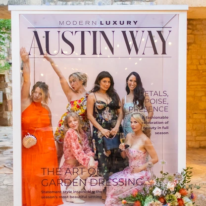 Group of five women posing behind an Austin Way magazine cover display at an event.