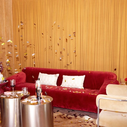 Living room with red velvet sofa, beige chairs, gold curtains, and metallic coffee tables with decorations.