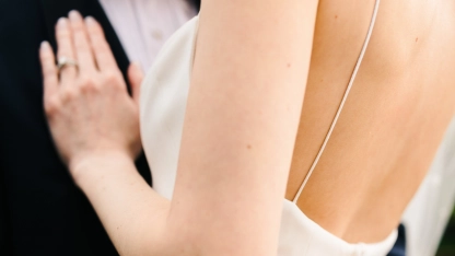 Close-up of a woman in a white dress with a backless design, holding hands with another person.