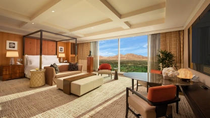 Spacious hotel suite with king bed, seating area, large windows, and desert mountain view.