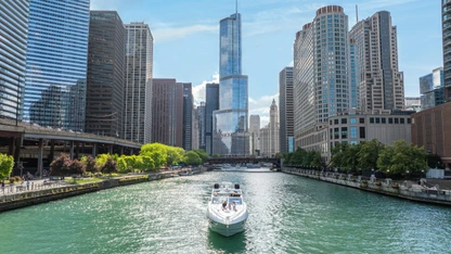 Boat cruising on Chicago River with skyscrapers and blue sky in the background.