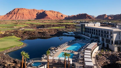 Resort with pool and hot tub near a lake, surrounded by rocky terrain and red mountains under clear sky.