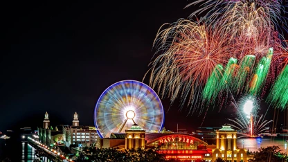 Nighttime fireworks display over Navy Pier with a lit Ferris wheel and illuminated buildings.
