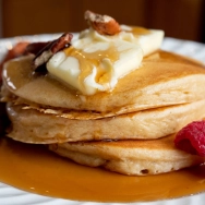Fluffy Pancakes with syrup whipped cream raspberry and blueberry on a white plate