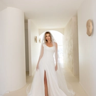 Bride in a white wedding dress with a front slit and veil standing in a minimalistic hallway.