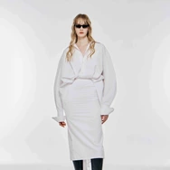 Woman wearing oversized white shirt, white midi skirt, black knee-high boots, and black sunglasses against white background.
