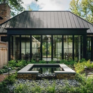 Modern garden patio with pond, surrounded by plants and a glass-walled building with a metal roof.