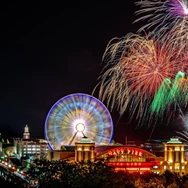 Nighttime fireworks display over Navy Pier with a lit Ferris wheel and illuminated buildings.