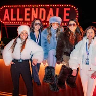 Five women wearing winter outfits posing at a bar with a bright ALLENDALE sign in the background.