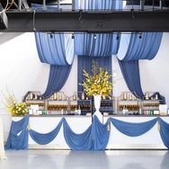 Event bar decorated with blue drapes, yellow floral arrangements, and elegant lighting fixtures.