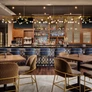Interior view of an empty modern bar with wooden tables, upholstered chairs, blue bar stools, and hanging lights.