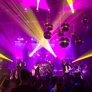 Live band performing on stage with purple and yellow lights and disco balls overhead.