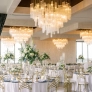 Elegant dining room with white tables, floral centerpieces, and crystal chandeliers, creating a refined atmosphere.