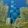 A tall, modern skyscraper surrounded by flowering trees and other buildings under a clear blue sky.