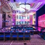 Modern banquet hall with purple lighting, geometric decorations, and long tables set for dining.