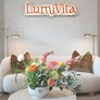 Cozy modern living room with white sofa, brown pillows, flower arrangement, and LumiVita sign on wall.
