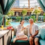 Couple relaxing and enjoying drinks by a poolside cabana with greenery and umbrellas around.