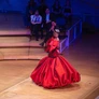 Flamenco dancer in a vibrant red dress performing on stage with seated audience in the background.