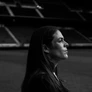 Black-and-white profile portrait of Kelley O’Hara on a soccer field, gazing forward with stadium stands blurred in the background.