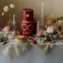 Elaborate dessert table with cakes, pastries, flowers, and lit candles in a vintage setting.