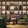 Modern living room with olive green armchairs, black side tables, and a large wooden bookshelf displaying decor and books.