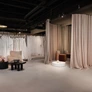 Interior of a bridal boutique with wedding dresses, fitting rooms with curtains, and seating area with chairs and tables.