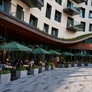 Outdoor cafe seating with green umbrellas beside a modern building with balconies and large windows.