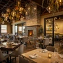 Cozy, upscale restaurant interior with warm lighting, fireplace, and elegantly set dining tables.