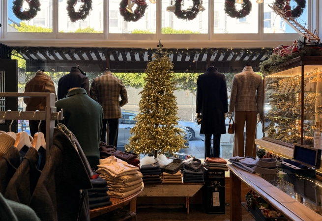 Mannequins dressed in winter clothing stand in a store decorated for Christmas with a tree and wreaths.