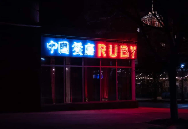 Neon sign at night reading 中国餐庁 RUBY on a dark street with a lit building dome in the background.