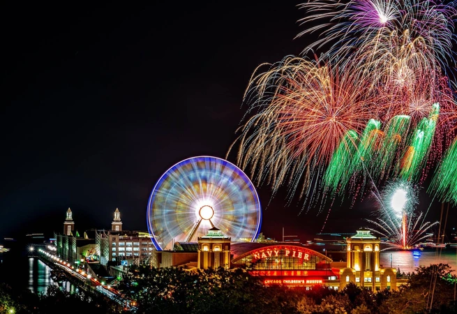 Nighttime fireworks display over Navy Pier with a lit Ferris wheel and illuminated buildings.
