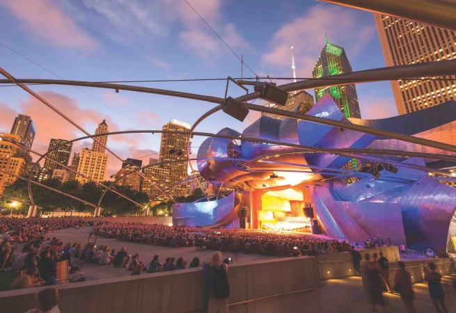 Outdoor concert at Jay Pritzker Pavilion in Chicago during sunset with city skyline background.