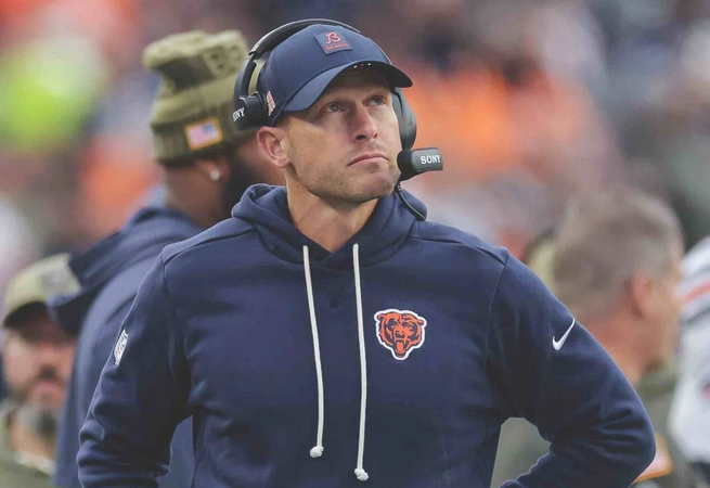 Coach wearing Chicago Bears hoodie and headset standing on football field during game.