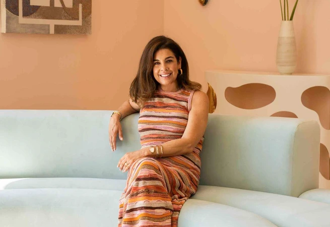 Woman smiling seated on curved light blue sofa in modern room with abstract art and vase of flowers.
