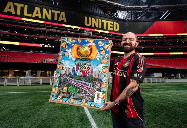 Man in Atlanta United jersey holding colorful Atlanta-themed artwork inside Mercedes-Benz Stadium.