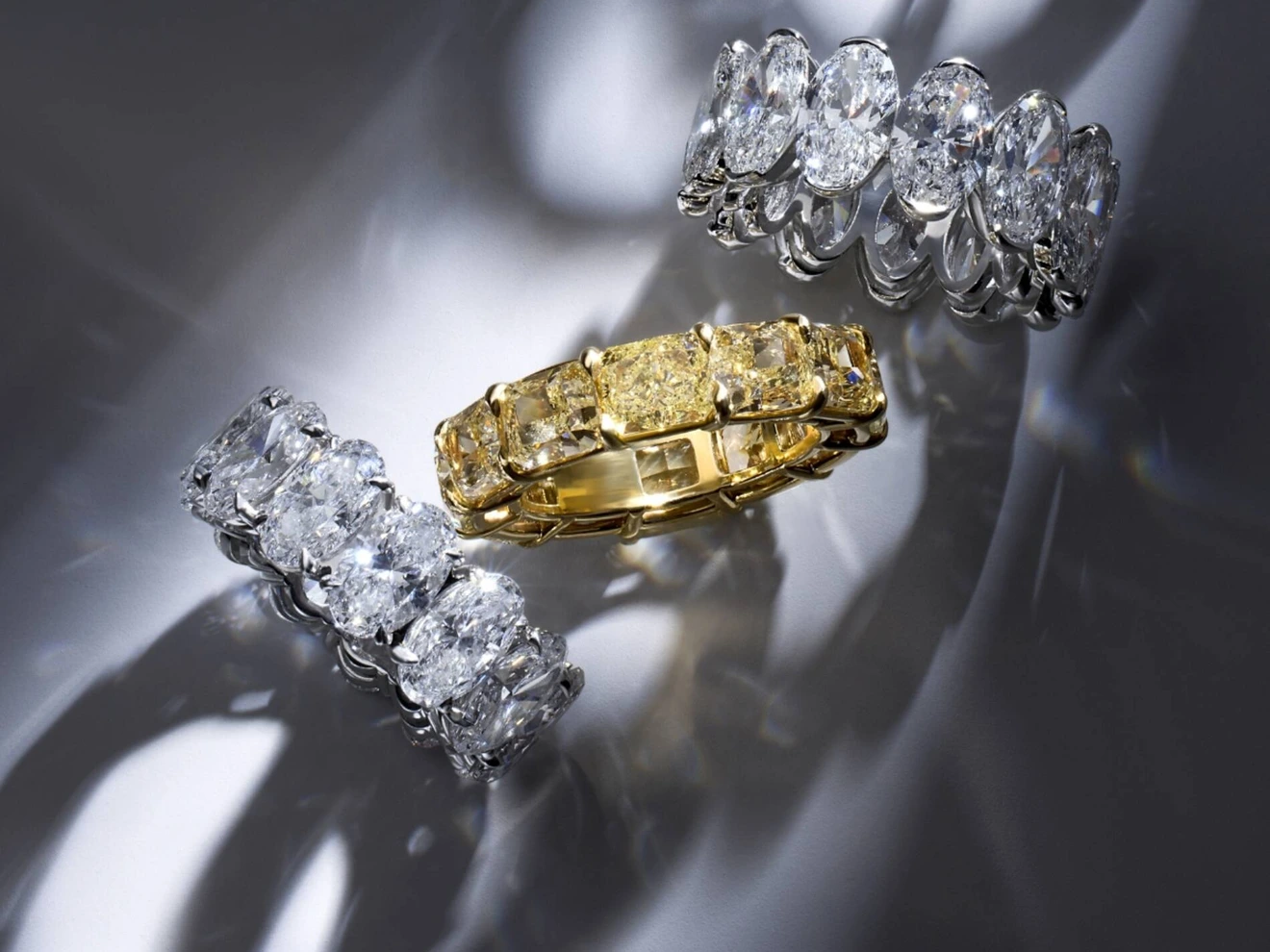 Three diamond-encrusted rings, two silver and one gold, displayed on a reflective surface.