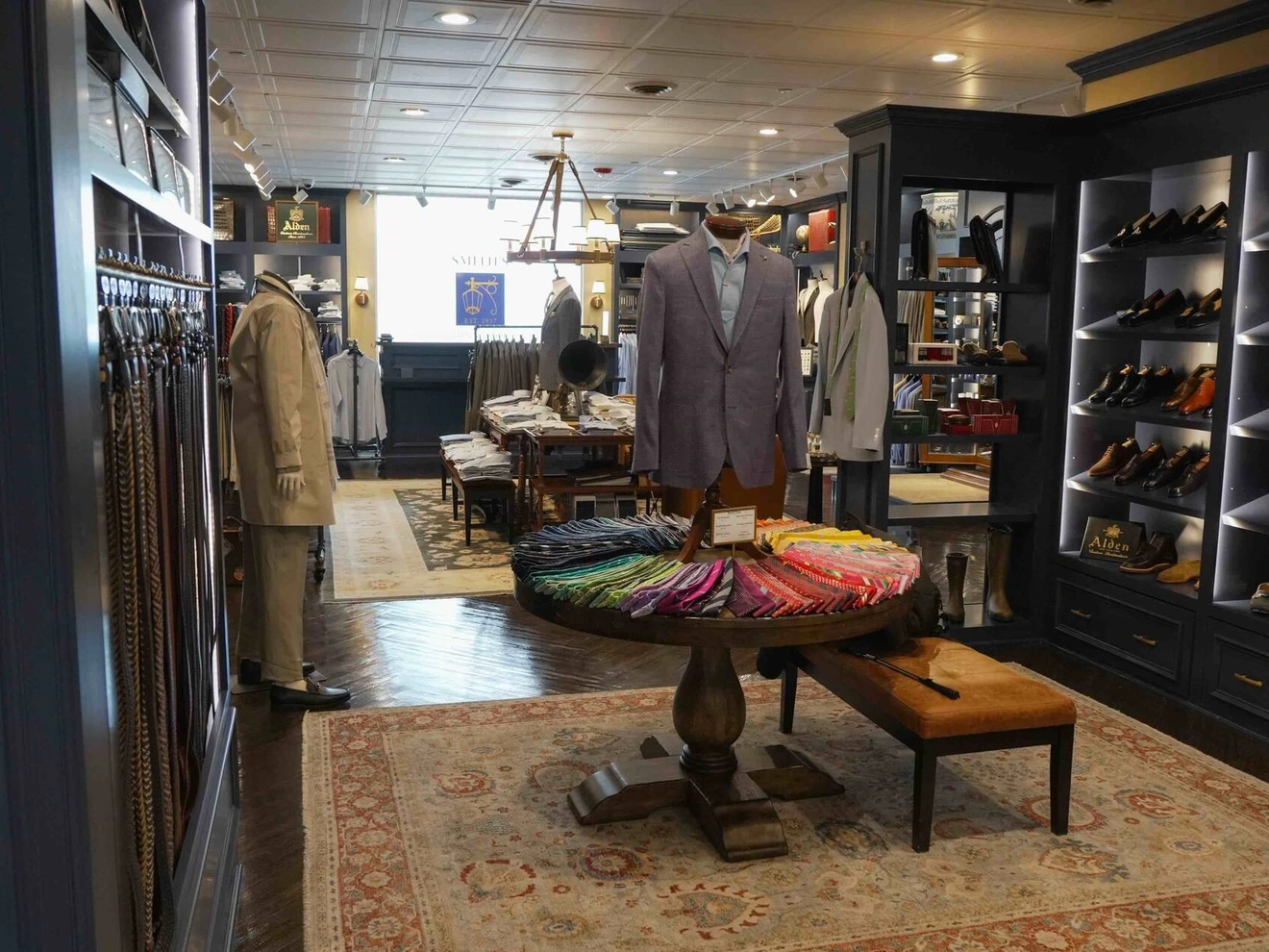 Interior of a men's clothing store with suits, shoes, and colorful ties displayed.