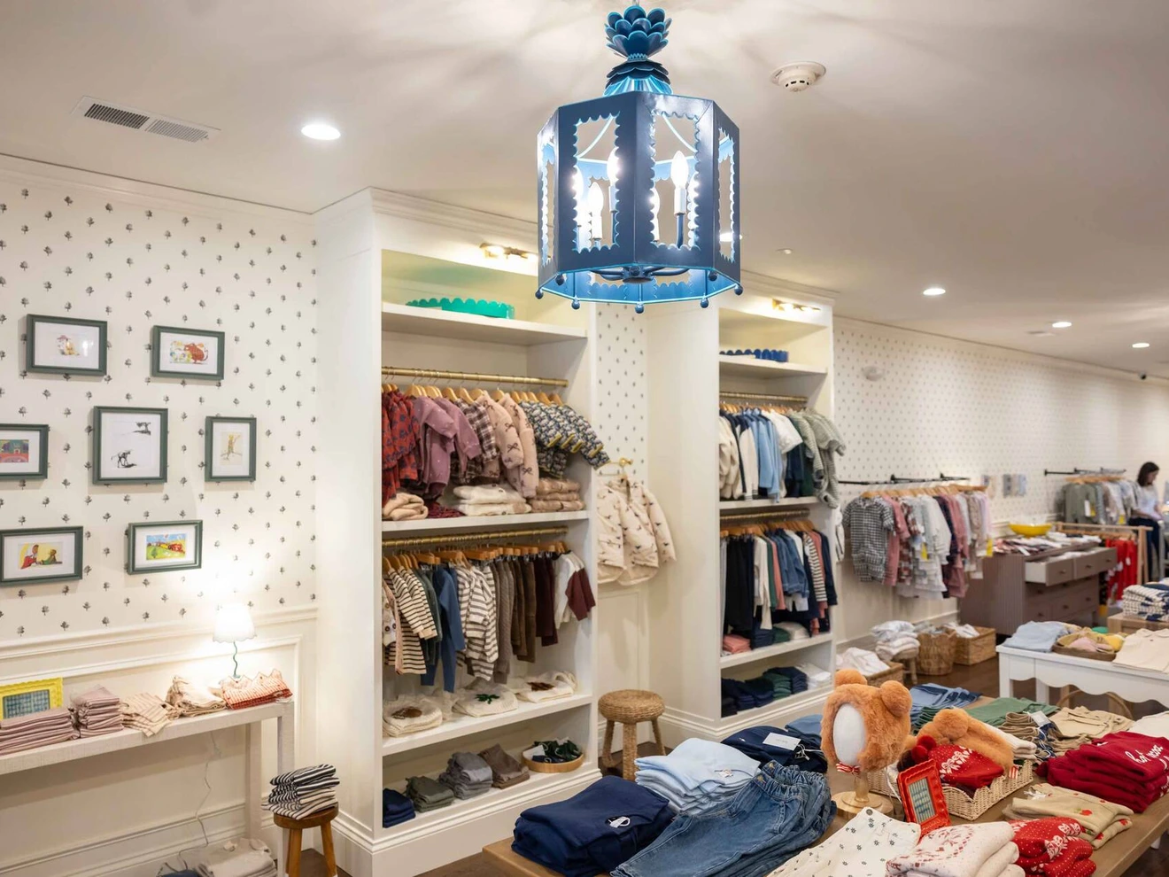 Interior of a children's clothing store with folded clothes, hanging outfits, and framed pictures on the wall.