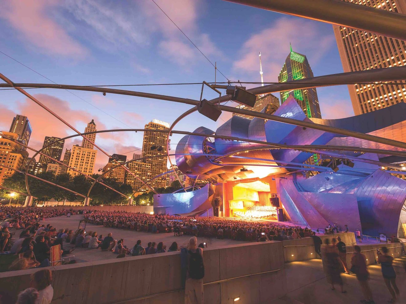 Outdoor evening concert at Jay Pritzker Pavilion, Millennium Park, Chicago with audience and city skyline.