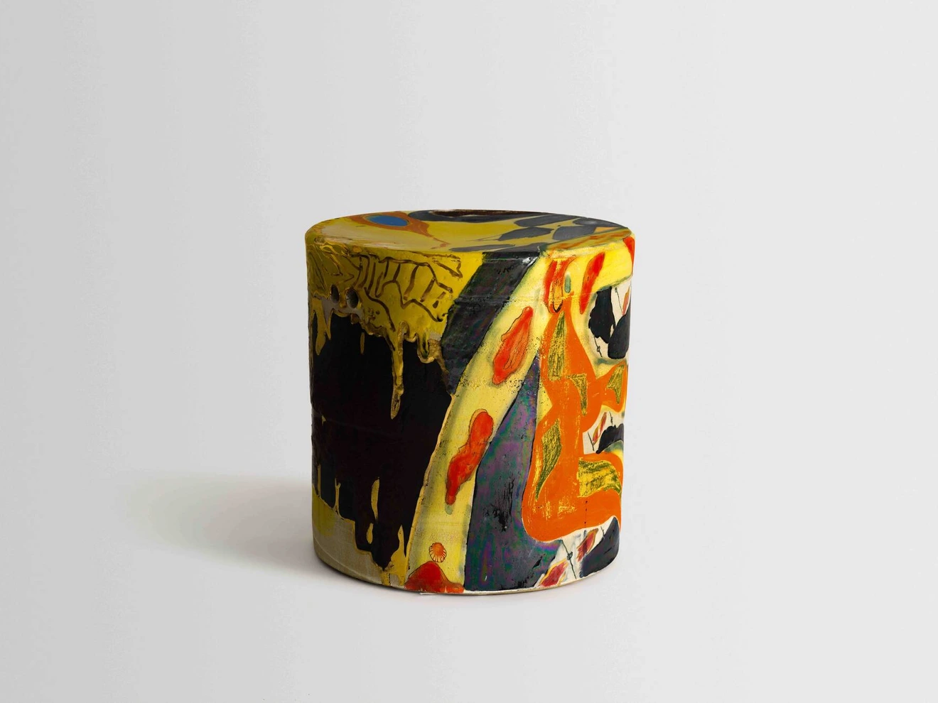 Colorful cylindrical ceramic object with abstract yellow, black, red, and orange painted design on a plain background.