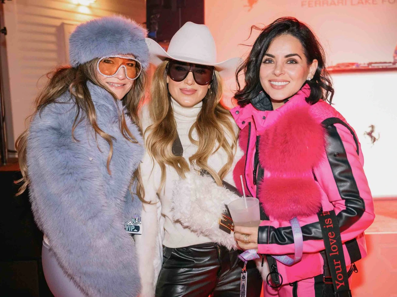 Three women dressed in colorful winter outfits posing and smiling indoors at an event.