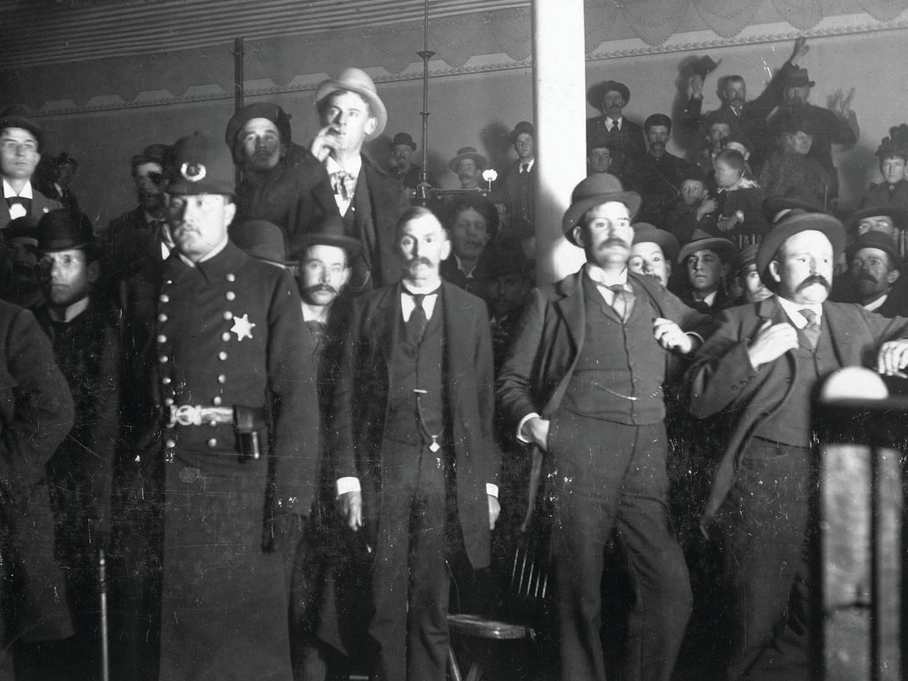 A group of men in suits and bowler hats bid on mining stocks during a night call at the Board of Trade and Mining Exchange in Colorado Springs. PHOTO COURTESY OF DENVER PUBLIC LIBRARY SPECIAL COLLECTIONS [P-1849]