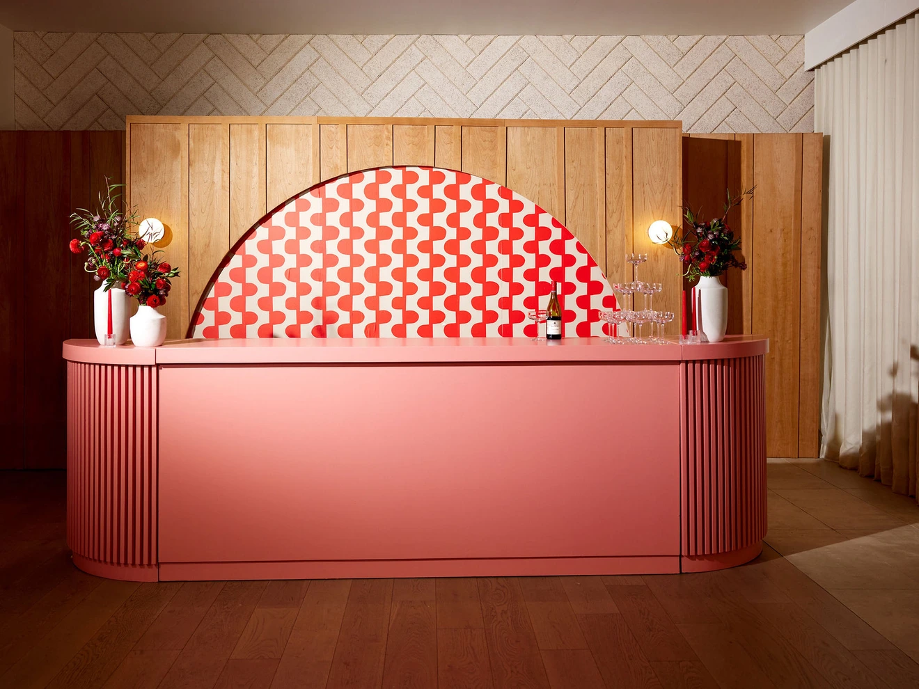 Modern pink curved bar counter with patterned backsplash and floral arrangements on both sides.