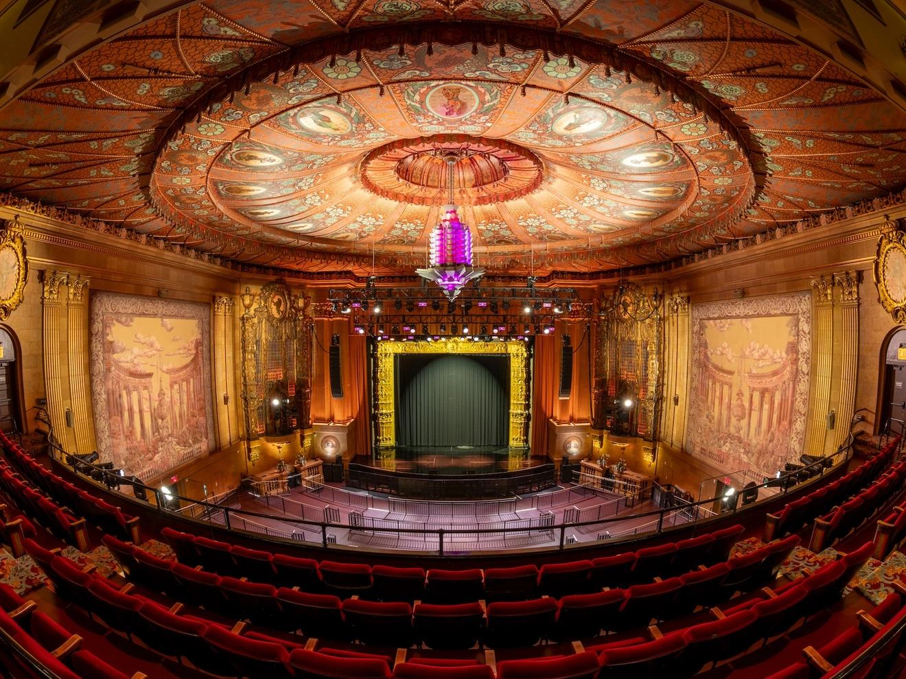 Interior view of an ornate vintage theater with a decorated ceiling and empty red seats.