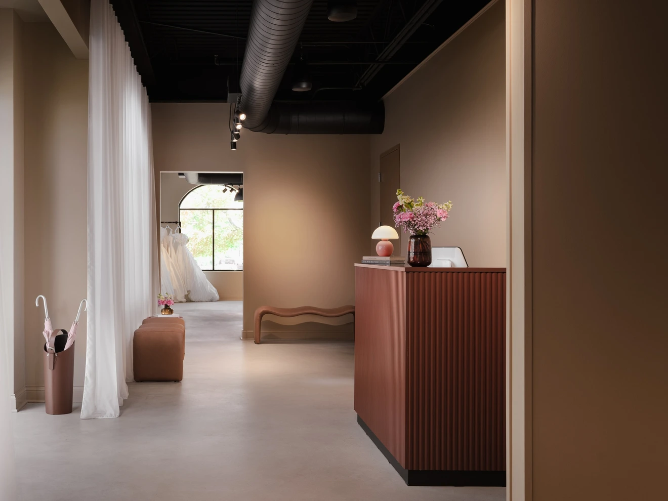 Interior of a modern bridal shop with brown walls, a reception desk, hanging dress, and soft natural light.