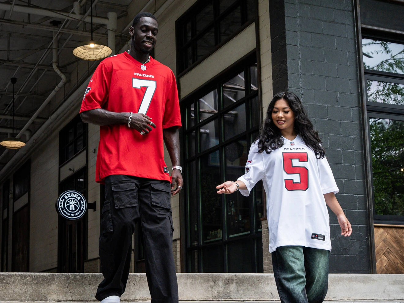 Two people wearing sports jerseys with numbers 7 and 5 walking down outdoor concrete steps.