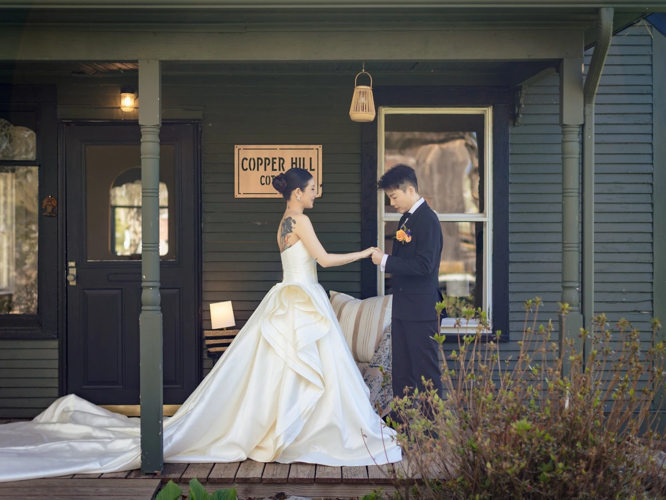 Bride and groom standing on a porch, holding hands in front of a Copper Hill sign.
